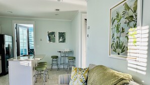 A living room with a sofa, a coffee table, and a kitchen area with a sink and stools. - Adorable Starlight EscapeCottage (Panama City Beach)