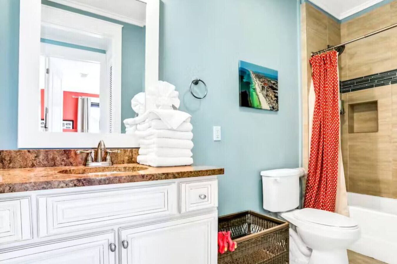 A bathroom with a marble sink, white cabinets, a toilet, and a shower with a red curtain.