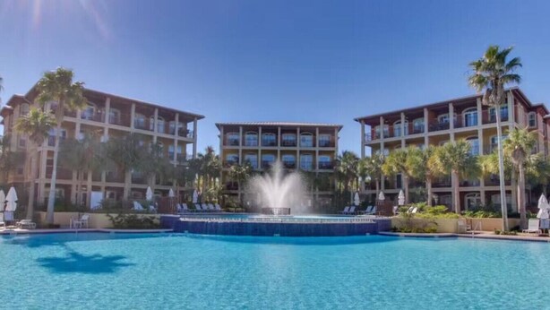 A hotel with a central pool and a fountain, surrounded by palm trees and multiple balconies. - Adorable Starlight EscapeCottage (Panama City Beach)