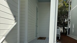 A white wooden staircase leading to a porch with a metal railing, surrounded by a wooden deck and a small garden area. - Adorable Starlight EscapeCottage (Panama City Beach)