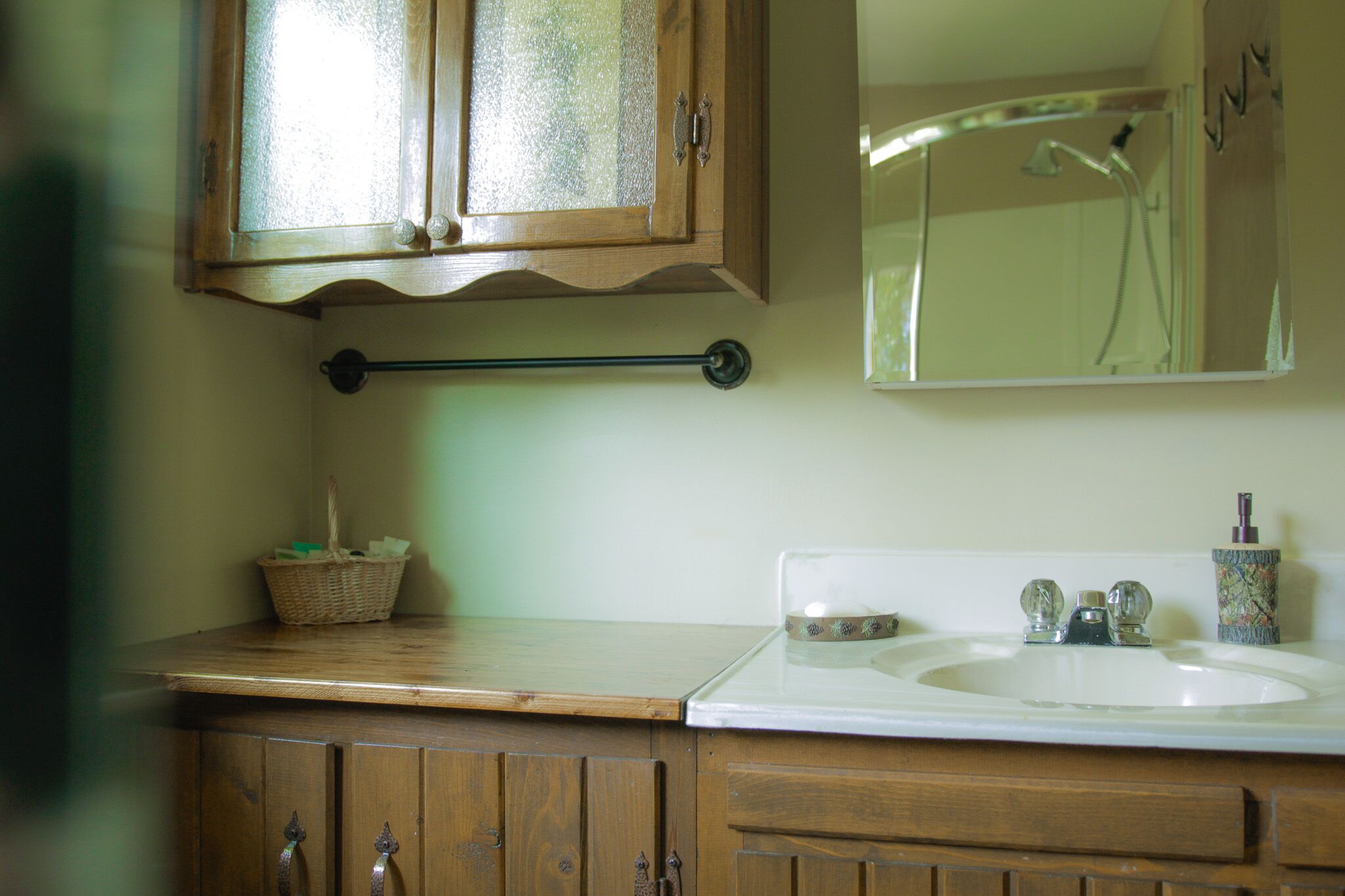 A bathroom with a wooden vanity, a white sink, a mirror, and a shower area.