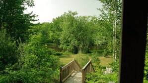 Eine Holzbrücke führt zu einem Teich, der von dichtem Grün umgeben ist.