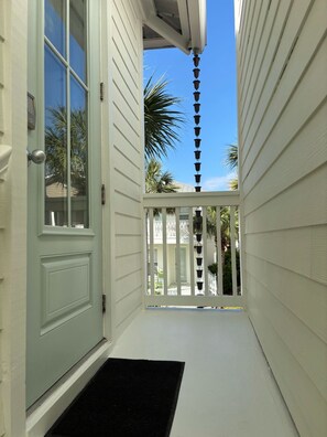 A narrow, white-walled corridor with a door and a small porch area.