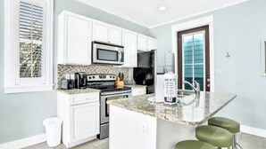 A kitchen with white cabinets, a microwave, a stove, a refrigerator, and a granite countertop. - Moonlight and Starlight Escape (Panama City Beach)
