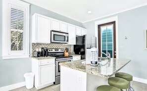 A kitchen with white cabinets, a microwave, a stove, a refrigerator, and a granite countertop. - Moonlight and Starlight Escape (Panama City Beach)