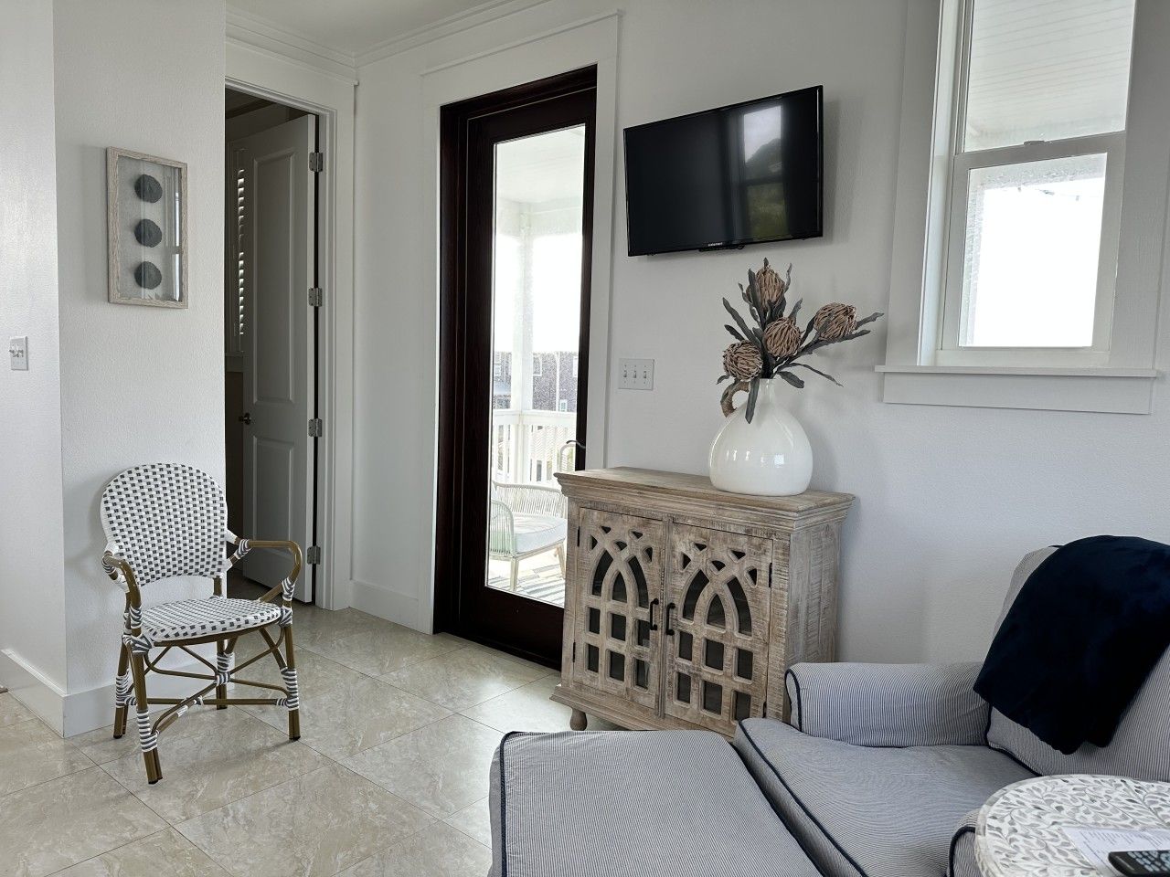 A living room with a wicker chair, a cushioned sofa, a wooden cabinet, and a television on the wall.
