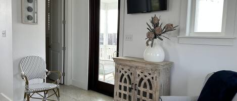 A living room with a wicker chair, a cushioned sofa, a wooden cabinet, and a television on the wall.