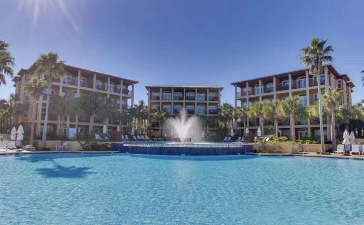 Un hôtel doté d’une piscine, de palmiers et d’une fontaine.
