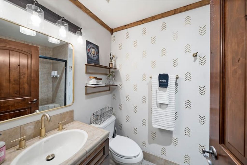 A bathroom with a large mirror, a sink, a toilet, and a shower area.