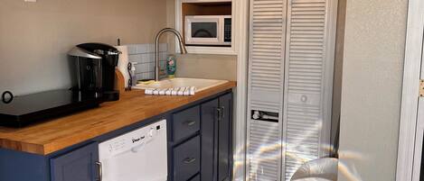 A compact kitchen with wooden cabinets, a built-in microwave, a coffee maker, and a dishwasher.