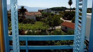 A view from a balcony with a blue railing, overlooking a residential area with houses, trees, and a clear sky. - Studio apartment in Sućuraj with Seaview, Balcony, Air condition, WIFI (3560-3) (Sucuraj)