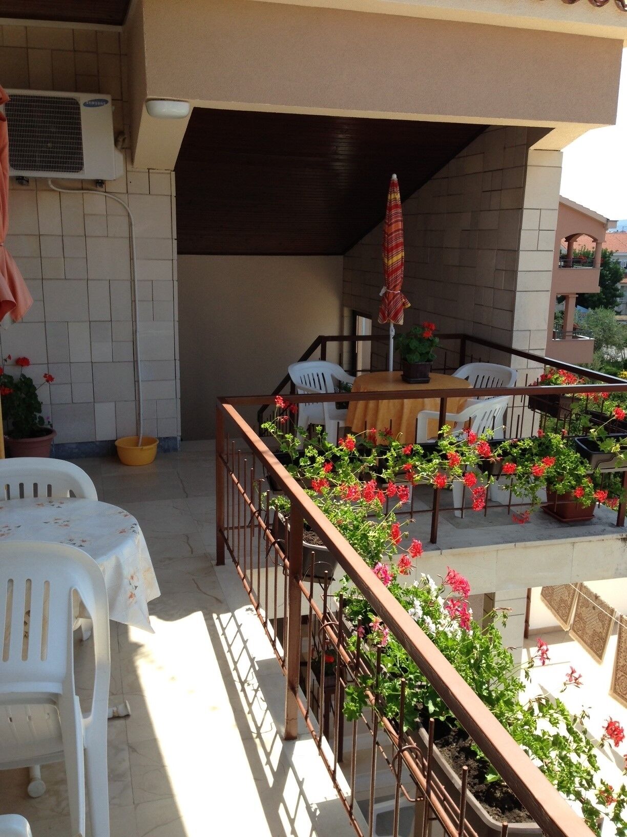 Un patio al aire libre con mesa y sillas, plantas en macetas y una barandilla.