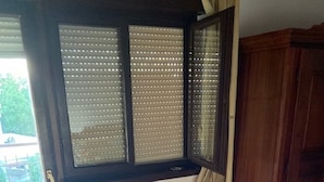 A room with a large window, a radiator, a wooden cabinet, and a herringbone-patterned floor.