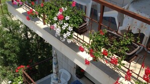 Ein mehrstöckiger Balkon mit Blumentöpfen und Blumen, weißen Stühlen und einem blauen Tisch.