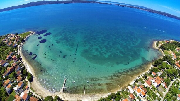 Vista aérea de una zona costera con aguas transparentes, una playa y edificios residenciales.
