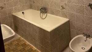 Un baño con bañera, inodoro y bidé. Las paredes están revestidas con un diseño geométrico.