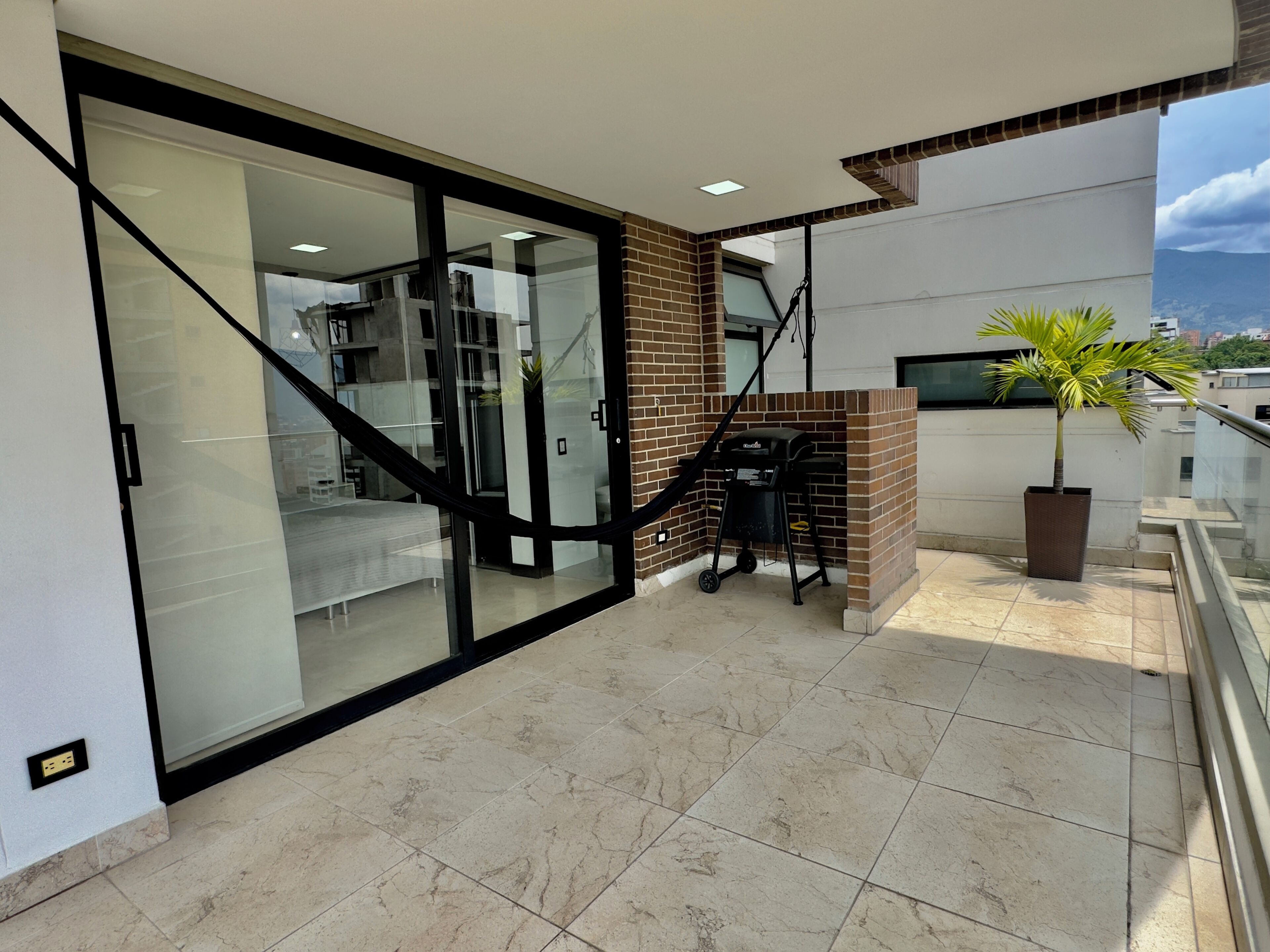 A modern interior with a glass door leading to a living area, a staircase, and a balcony with a grill and a potted plant.