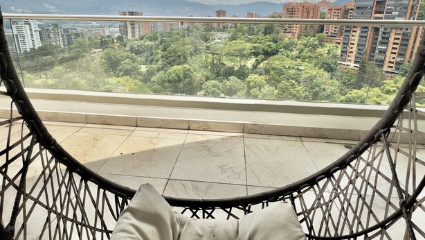 Vista da un balcone con ringhiera in metallo su un panorama urbano con edifici e aree verdi.