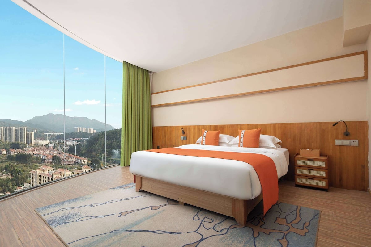 Une chambre d’hôtel moderne avec un grand lit, une tête de lit en bois et une vue sur le paysage urbain.