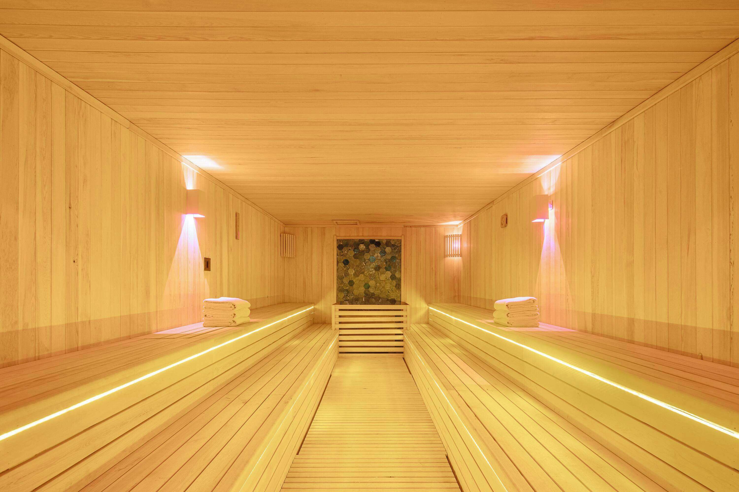 Una sauna con bancos de madera, un pasillo central y luces fijadas a la pared.