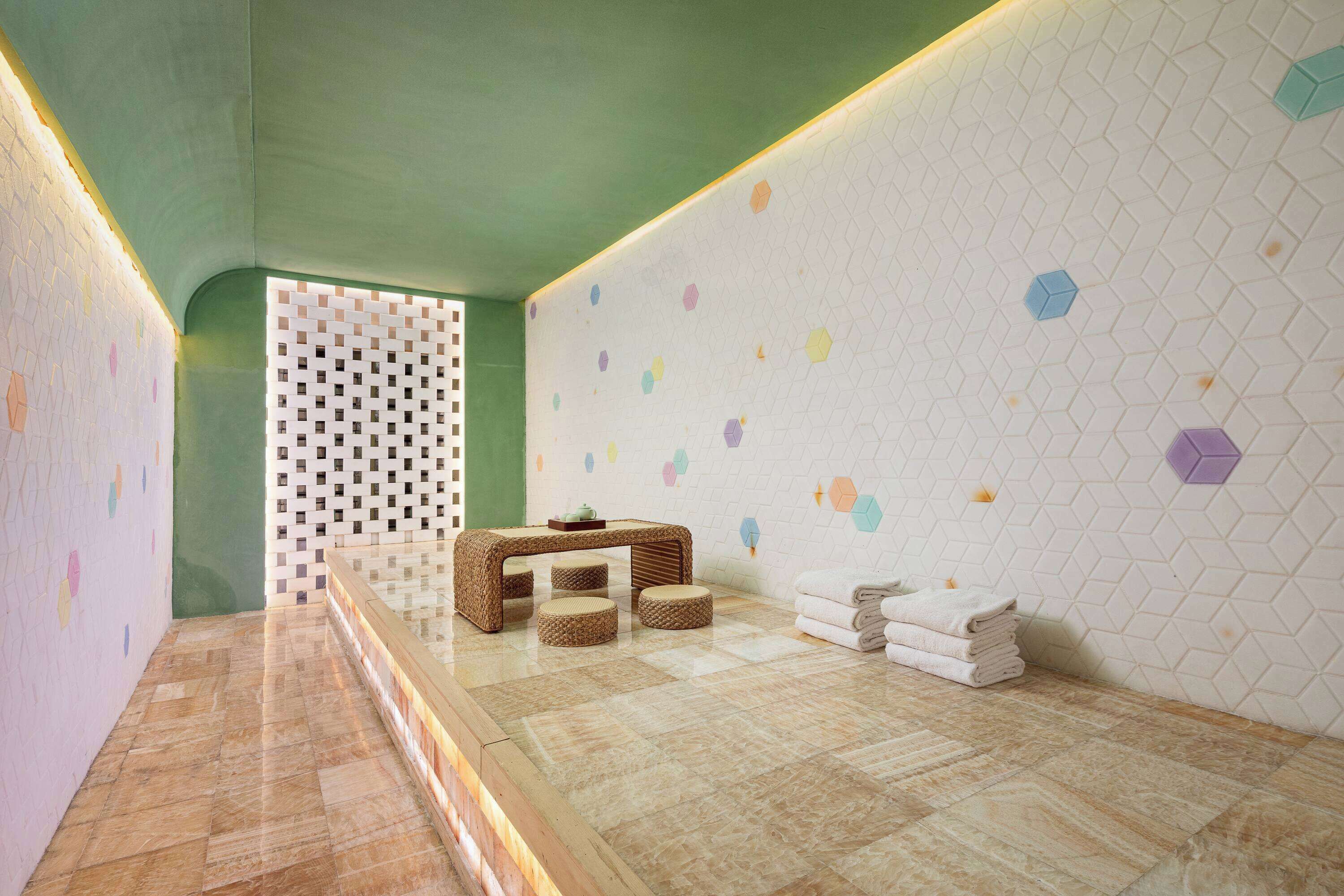 Um espaço de spa com piso de madeira, um banco de fibra natural e parede com desenhos hexagonais.