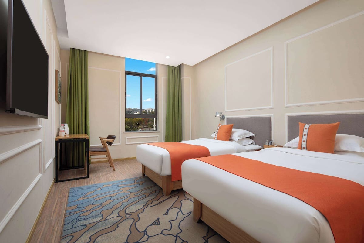 Une chambre d’hôtel avec deux lits, une télévision, une petite table et une fenêtre donnant sur un paysage agréable.