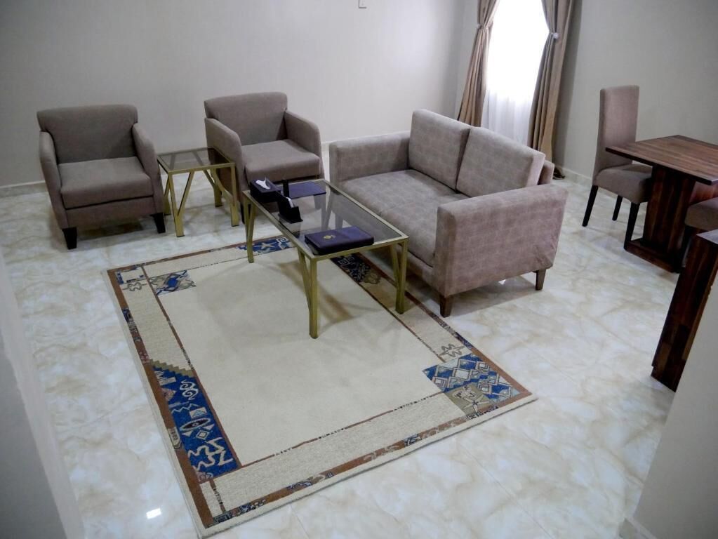 Una sala de estar con un sofá color beige, dos sillones, una mesa de centro de vidrio y una alfombra estampada.
