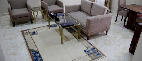 Una sala de estar con un sofá color beige, dos sillones, una mesa de centro de vidrio y una alfombra estampada.