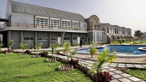 A modern hotel with a swimming pool, a well-maintained lawn, and a large building with a curved roof.