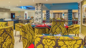 A dining area with yellow patterned chairs, a pool table, and a bar area with a counter.
