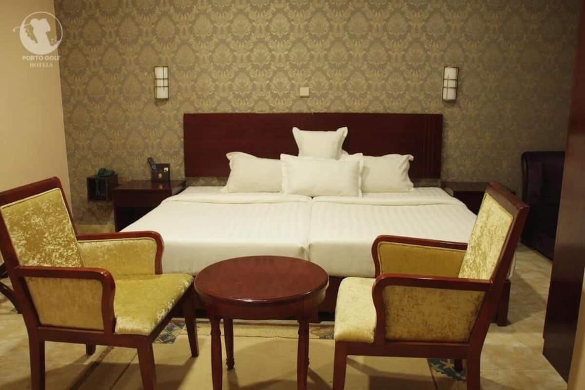 Hotelkamer met een groot bed, twee fauteuils, een klein rond tafeltje en behang met een patroon.