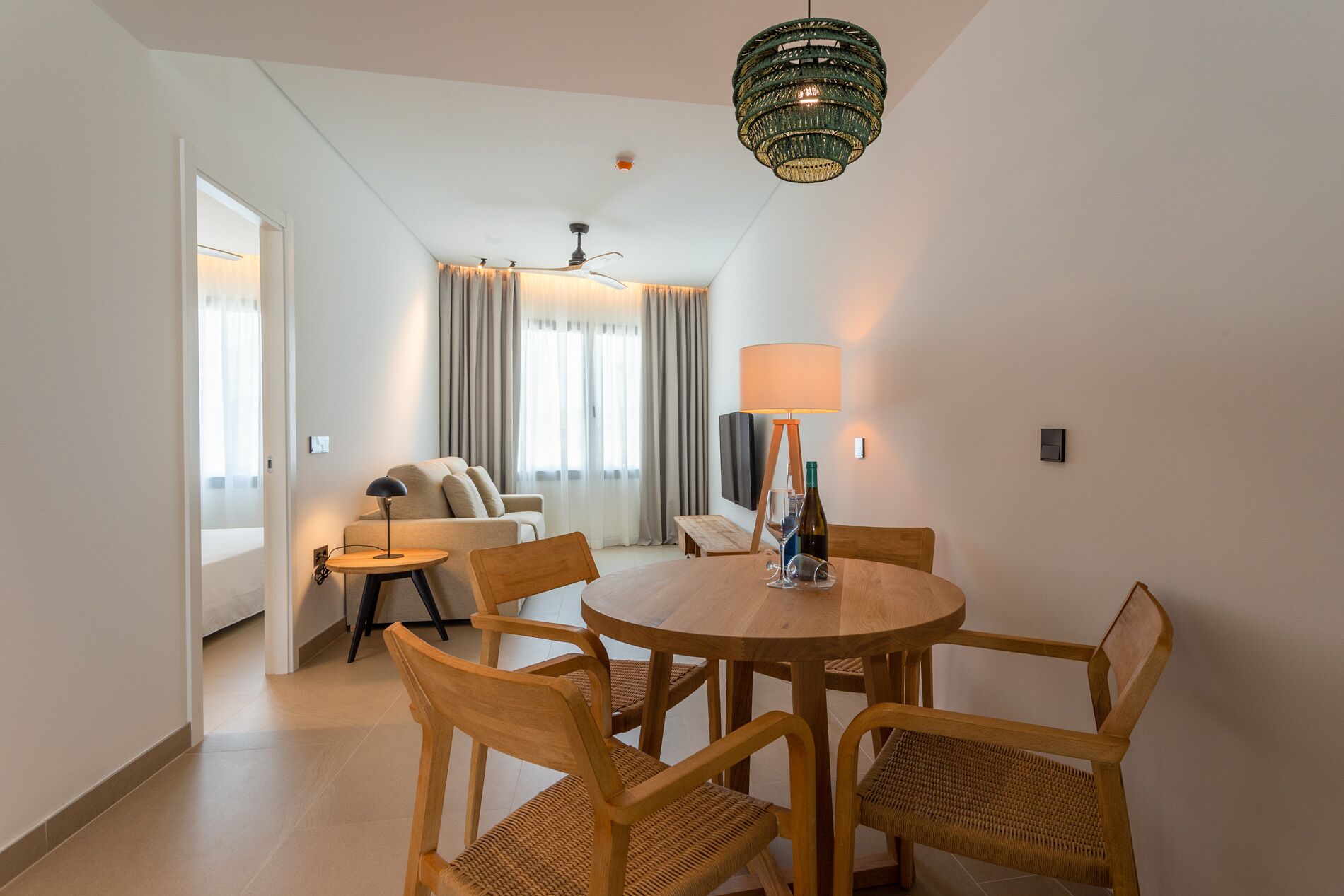 Una sala de estar moderna con una mesa redonda de madera, cuatro sillas de mimbre, un sofá, un televisor y una lámpara de araña decorativa verde.
