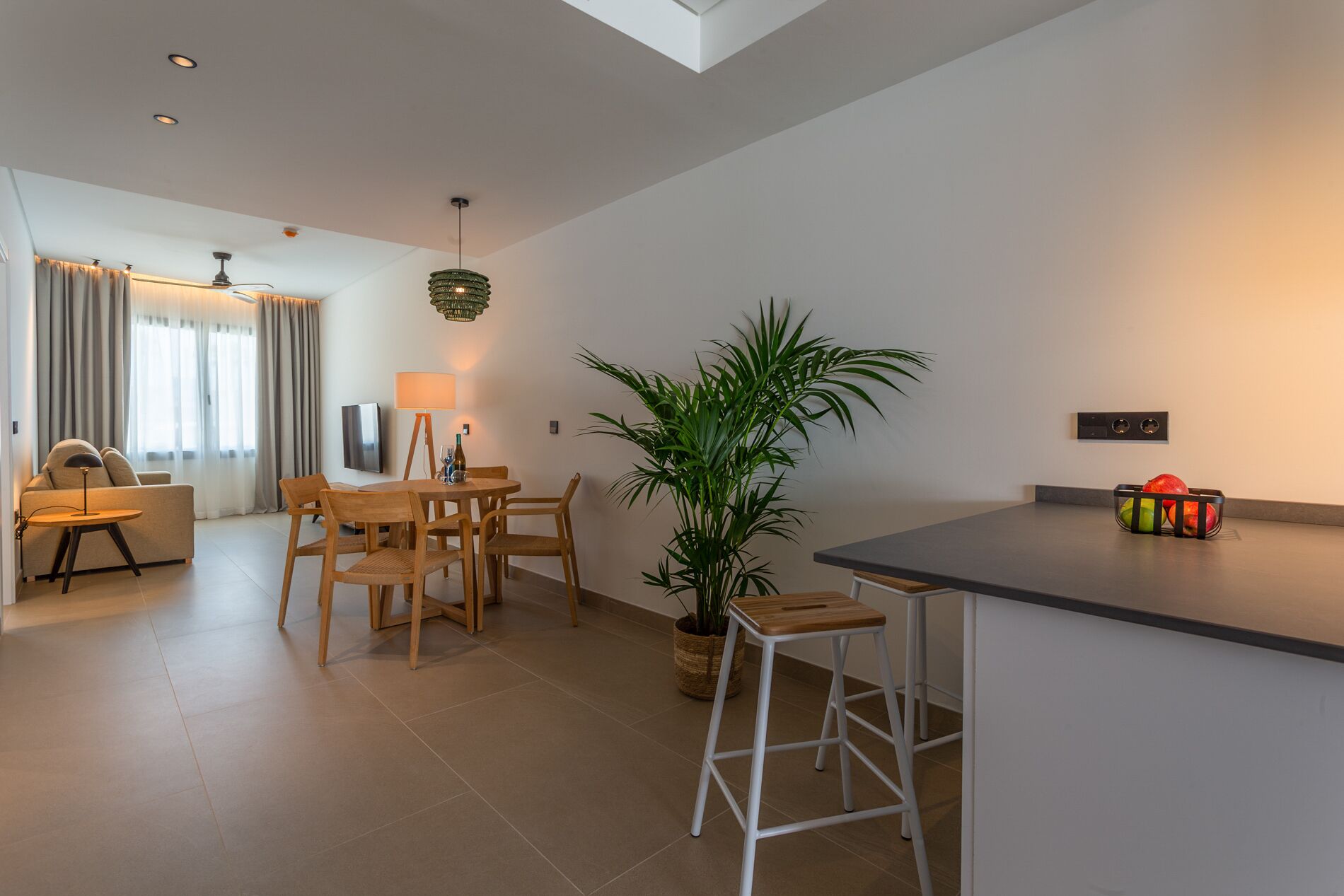 A modern kitchen with a central island, wooden chairs, a dining table, and a potted plant.