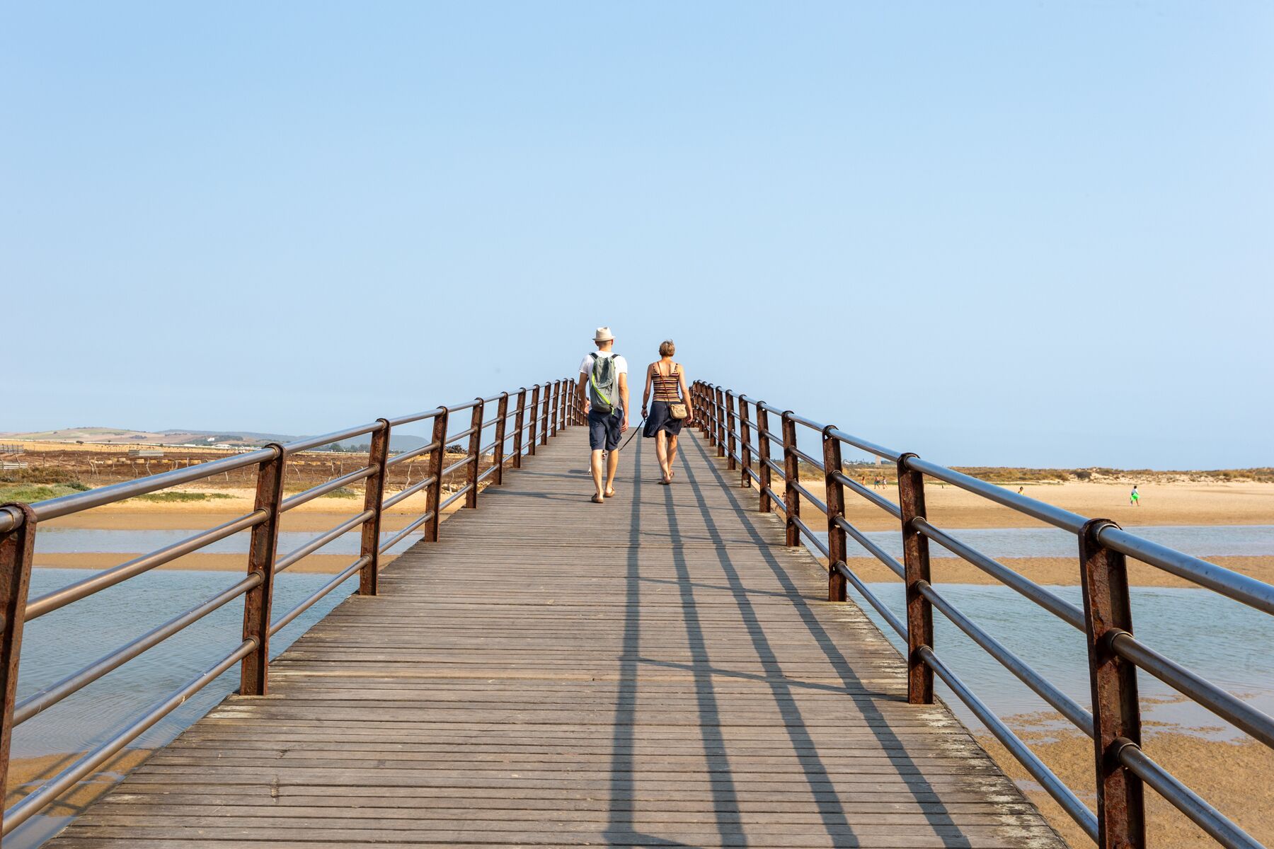 A wooden pier with metal railings leading to a beach.