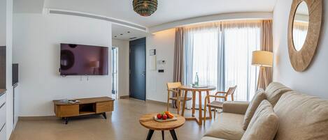 Ein modernes Wohnzimmer mit einer Couch, einem Couchtisch mit Obst, einem Fernseher und einem Essbereich mit Stühlen und einem Tisch.