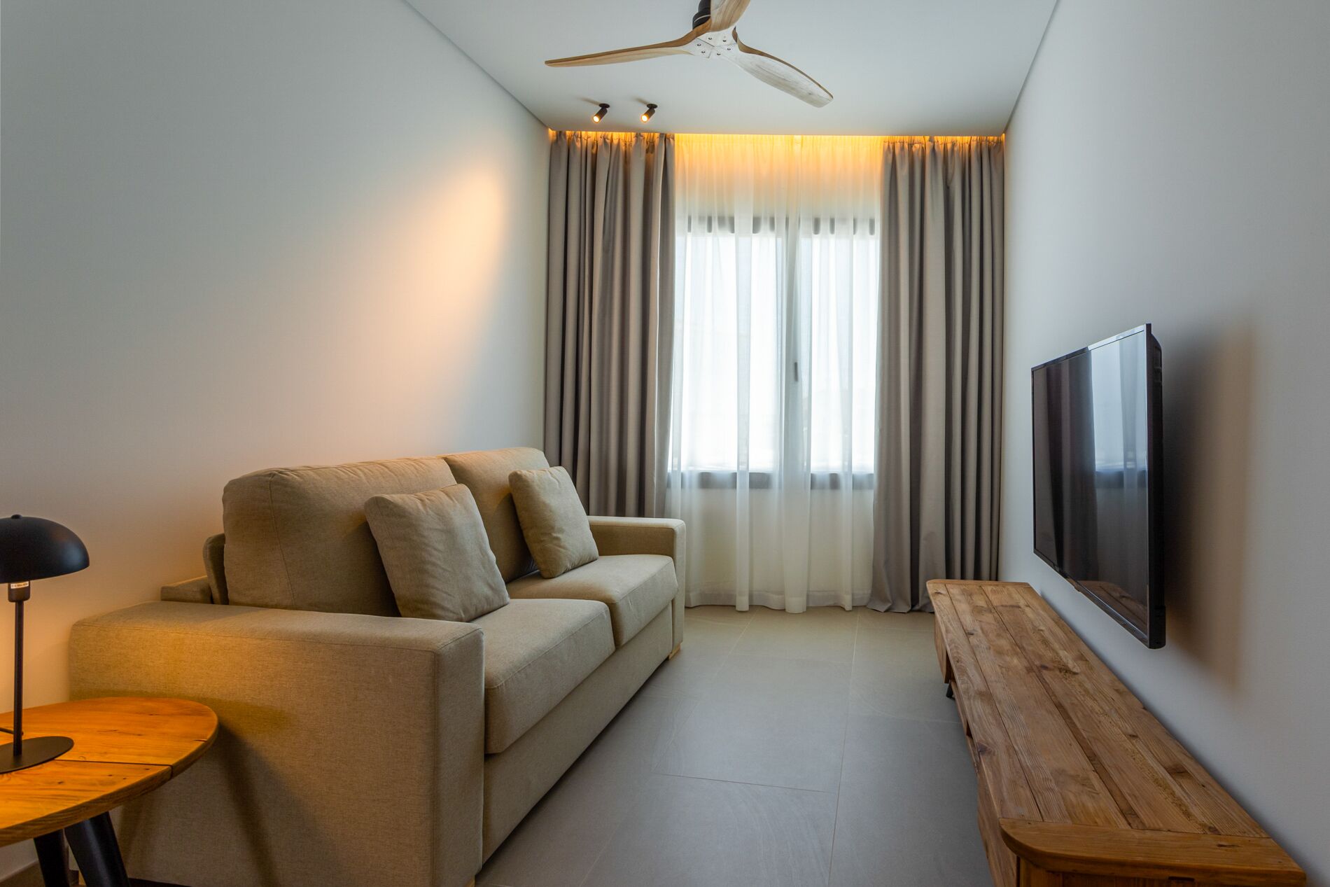 A modern living room with a sofa, a wooden bench, a TV, and a ceiling fan.
