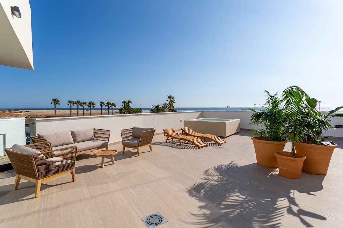 A rooftop terrace with wicker furniture, a hot tub, and potted plants.