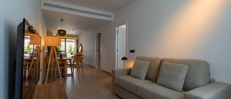 A modern living room with a sofa, wooden floor, and a dining area with a table and chairs.