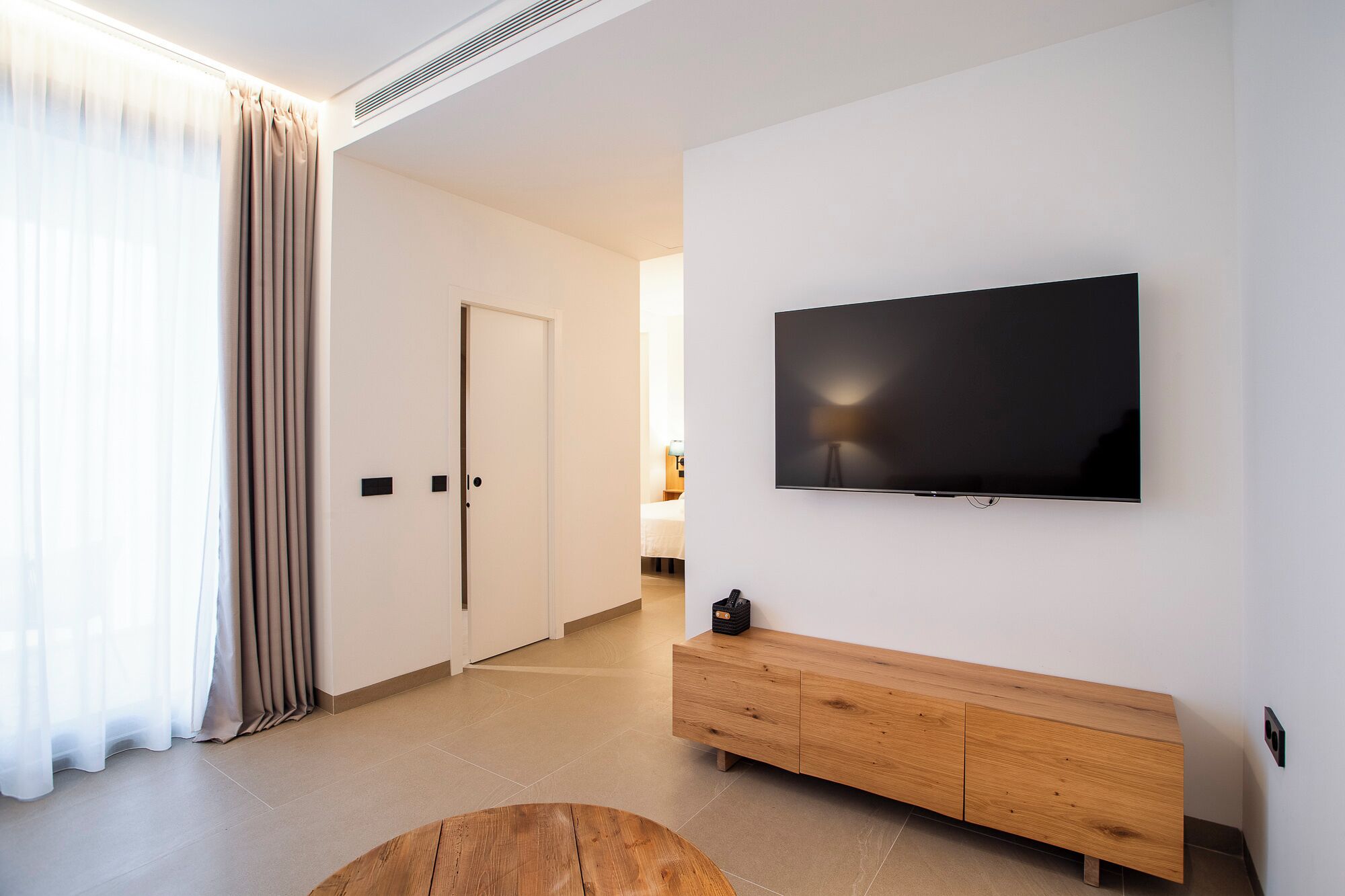 A modern hotel room with a flat-screen TV mounted on the wall, a wooden console table, and a large window with curtains.