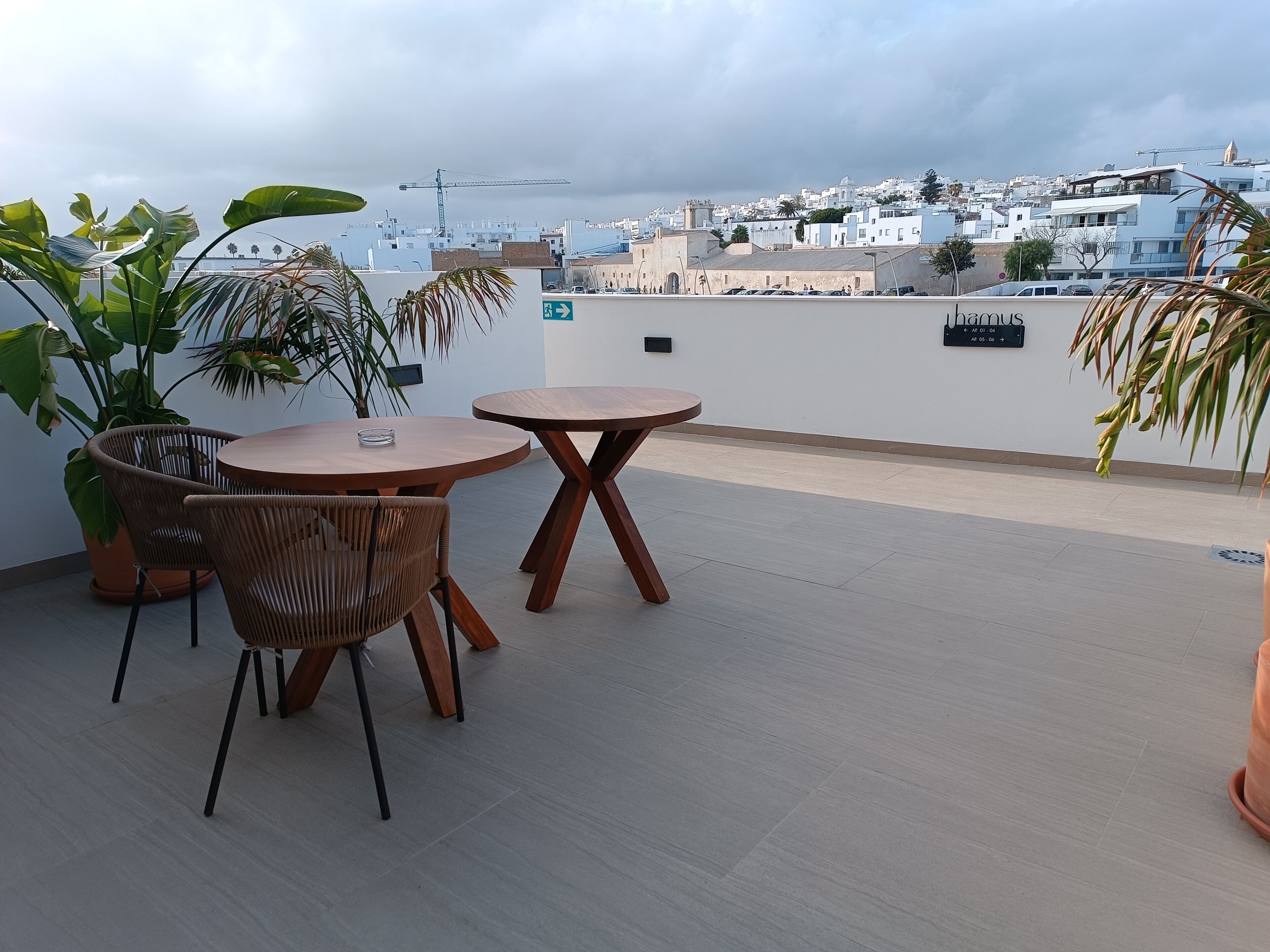 A rooftop terrace with a round wooden table and chairs, surrounded by potted plants.