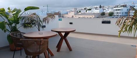 A rooftop terrace with a round wooden table and chairs, surrounded by potted plants.