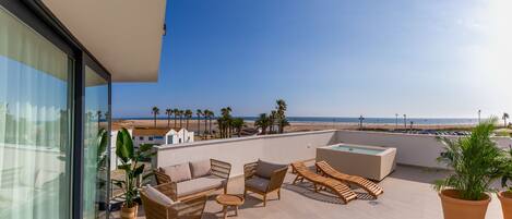 Eine Dachterrasse mit Korbmöbeln, einem Whirlpool und Blick auf den Strand und Palmen.