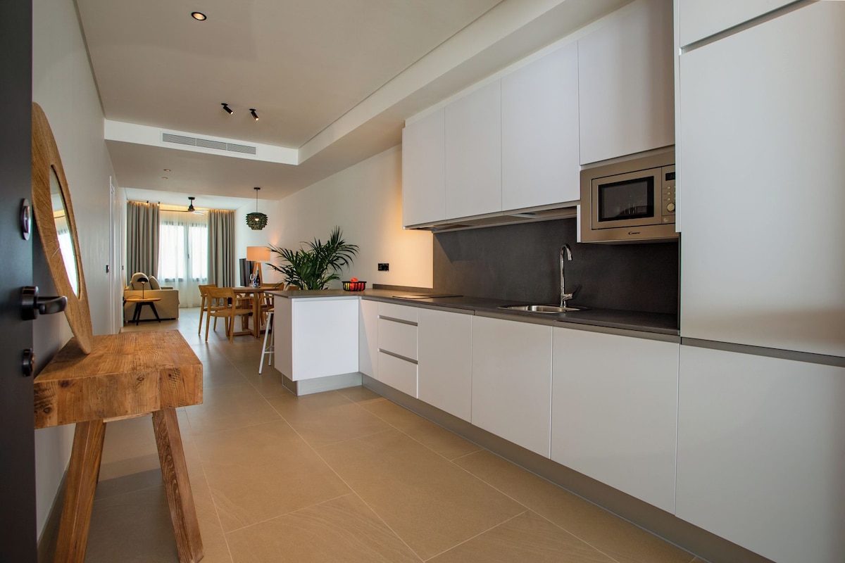 A modern kitchen with white cabinets, a stainless steel microwave, and a dining area with a table and chairs.