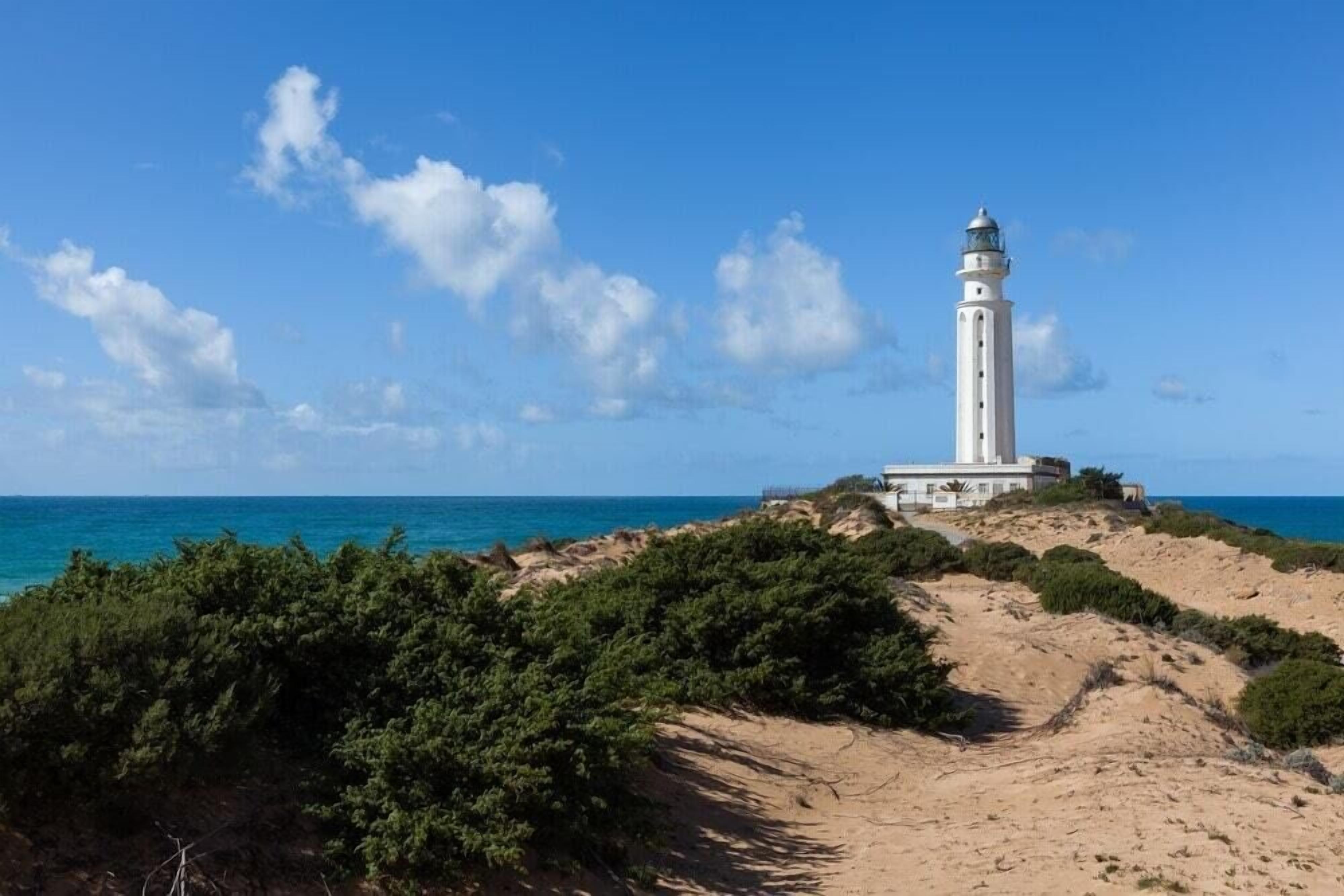 A lighthouse on a sandy hill with a clear view of the ocean.
