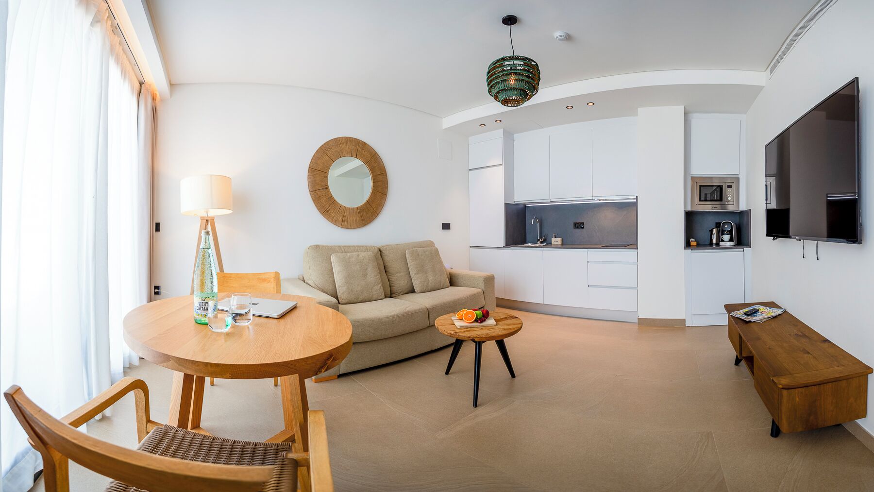A modern living room with a round wooden table, a sofa, a small wooden side table, and a dining area with a chair.