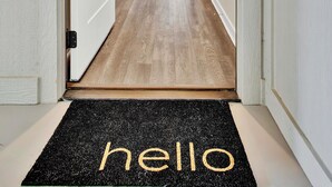 Een gang met een zwarte deurmat waarop ‘hello’ staat, een houten deur en het getal ‘201’ op de muur.
