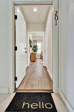 Enter a welcoming space with a doormat reading 'hello' and a hallway leading to a room with a window and a plant.