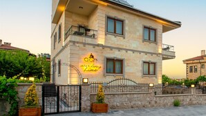 A two-story building with a balcony, a neon sign, and a stone facade. - Cappadocia Acer Living Home (Ürgüp)