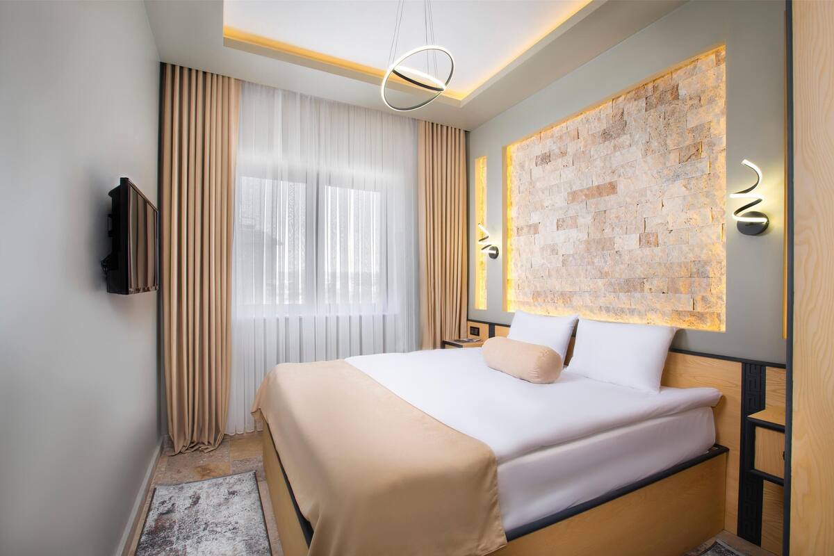 A modern hotel room with a large bed, a flat-screen TV mounted on the wall, and a decorative wall panel.