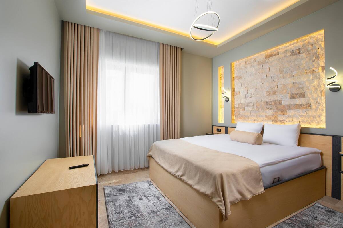 A modern hotel room with a large bed, a bedside table, a flat-screen TV, and a decorative wall panel.